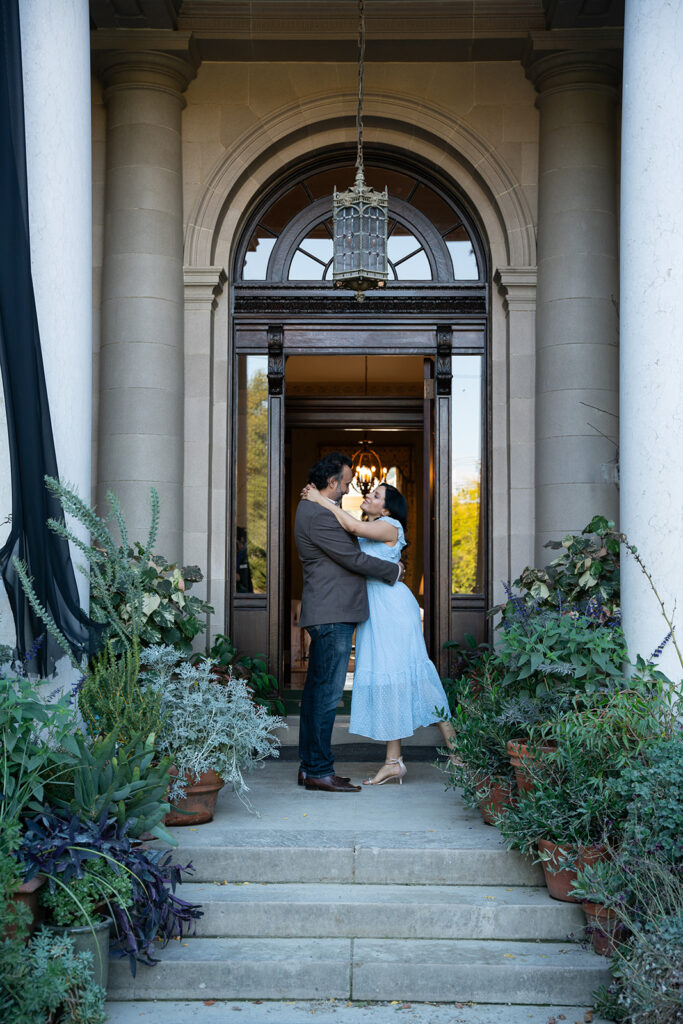 Indian couple standing in front of the Filoli Gardens Museum entrance staring into each other's eyes. The woman is dressed in a light blue dress and the man is wearing a grown blazer and dark blue washed jeans