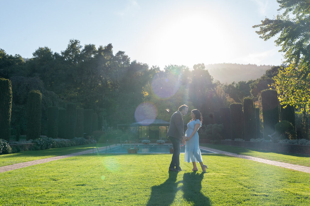 Indian couple holding hands and dancing in an open grass field with their shadows dancing along with them during high noon and they are both smiling at one another
