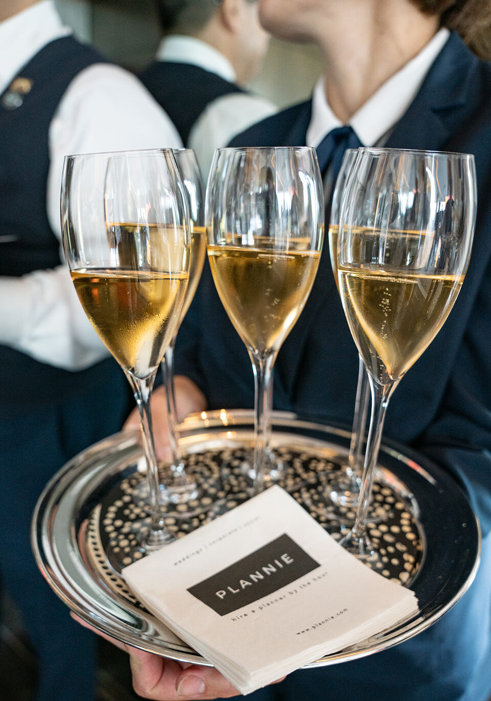 Five champagne glasses on a tray with the napkins being held by a waiter