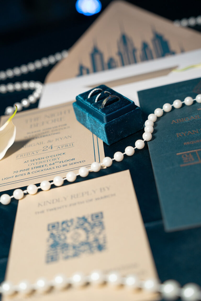 Wedding detail shots in editorial style with pearls, wedding bands, and a mix of blues and beige in the stationary items with flash